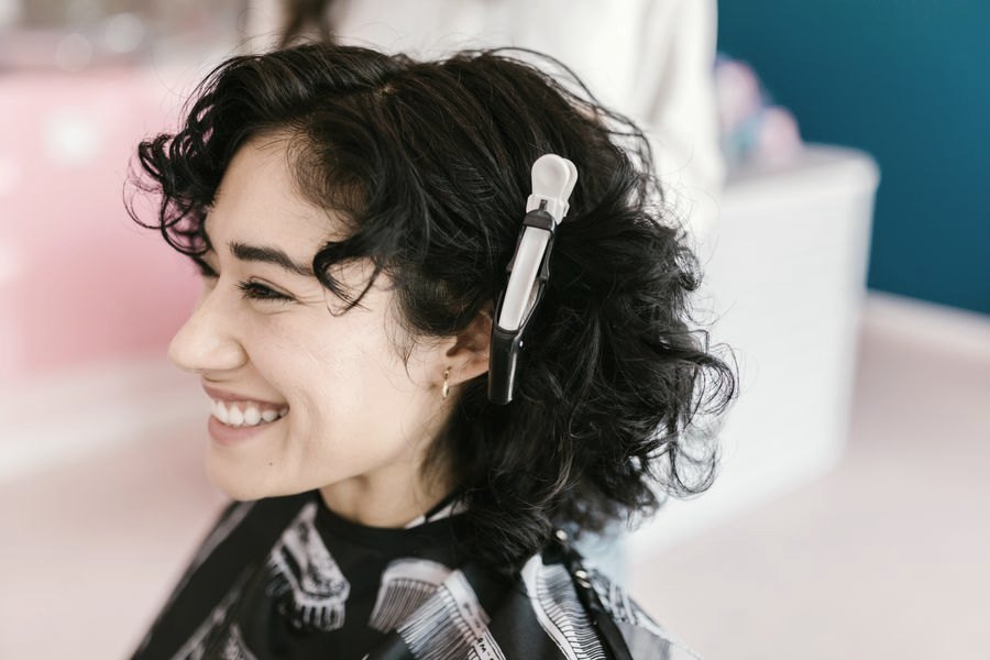 Cliente sorrindo de perfil com cabelo cacheado preso por presilha