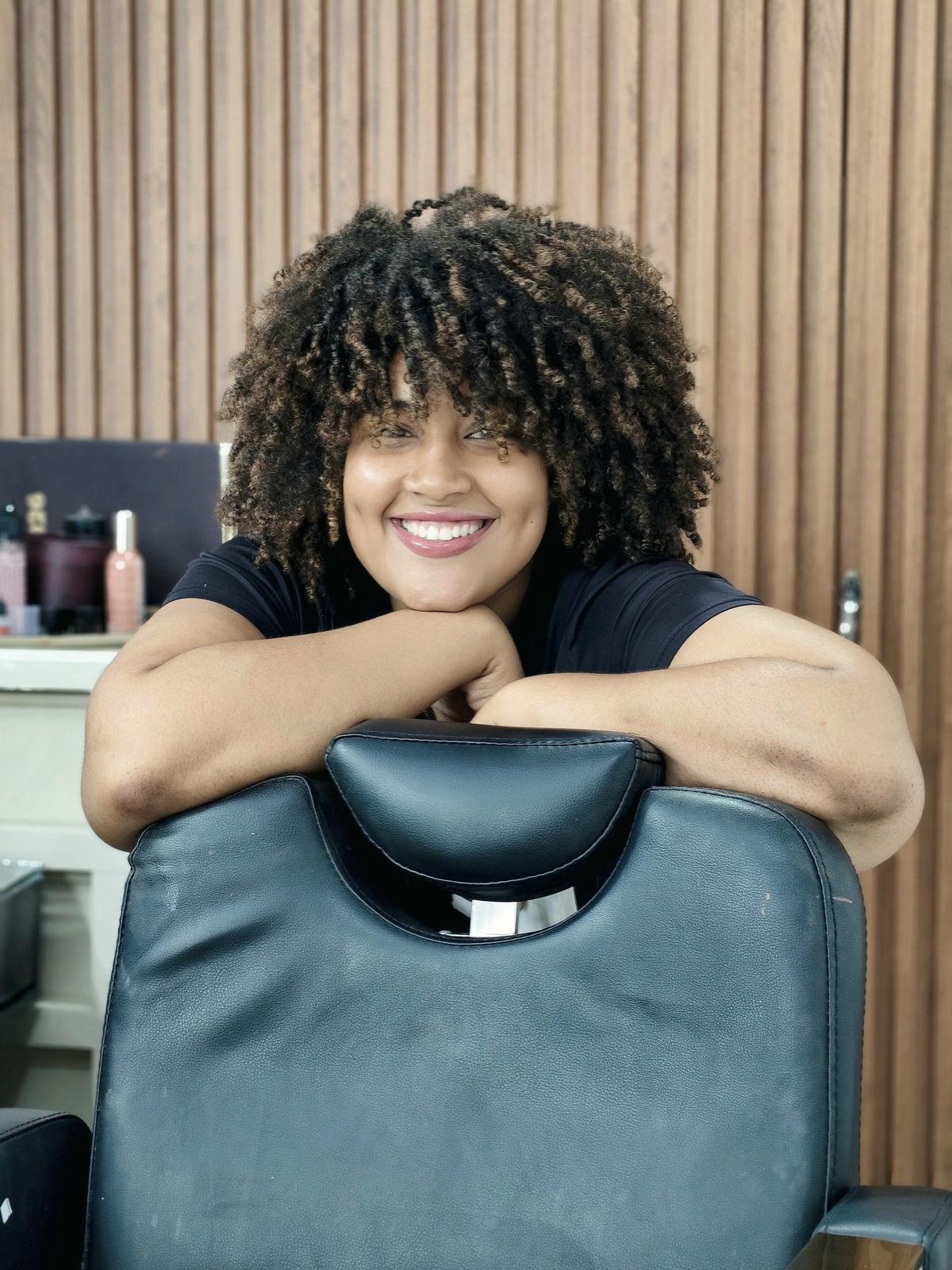 Cliente sorridente de cabelo cacheado apoiada na cadeira do salão