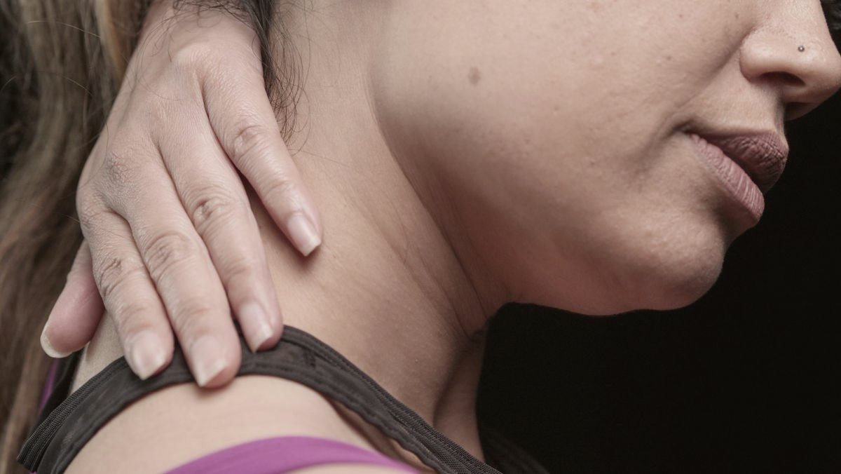 Mulher levando a mão ao pescoço, indicando dor cervical